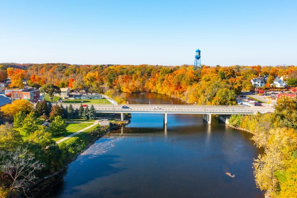 Aerial view of Grand Ledge, Michigan, featuring the Bridge Street bridge over the Grand River surrounded by vibrant autumn foliage.