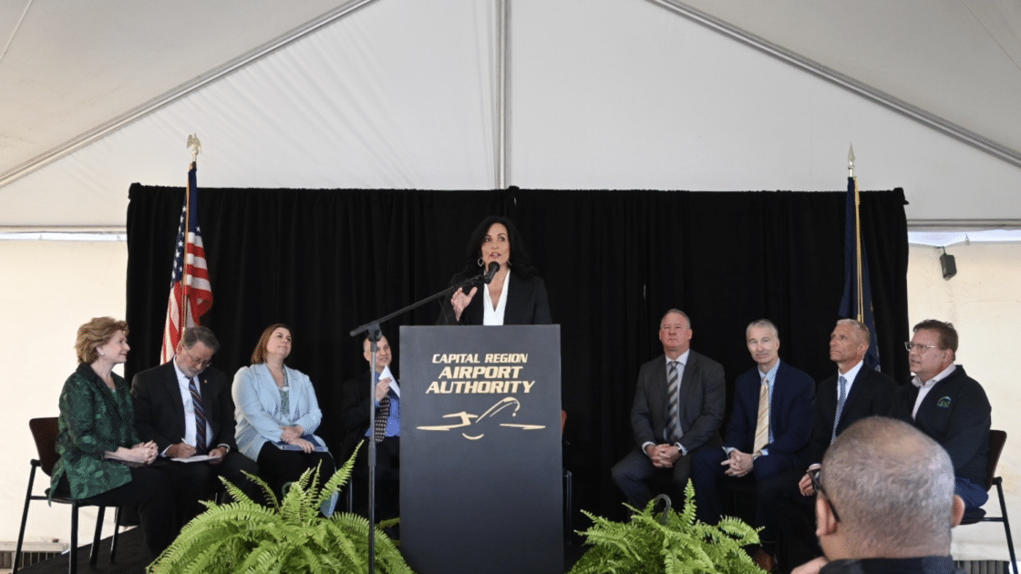 A picture showing Capital Region Airport Authority President & CEO Nicole Noll-Williams speaking at an airport event on April 11 to announce the expansion of the airport’s cargo ramp and Niowave’s Port Lansing location. Several individuals are seated on stage with the speaker.