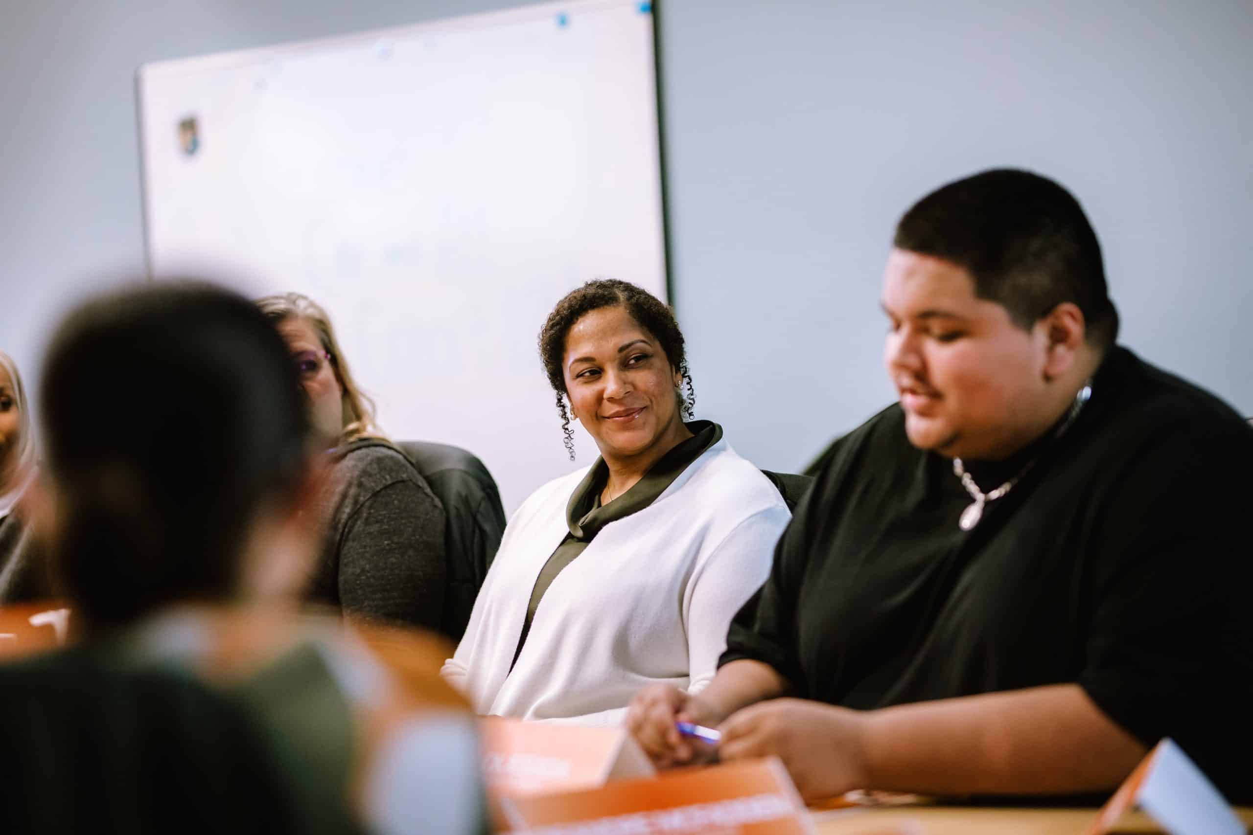 A woman smiles while listening to a colleague during a group workshop or meeting.