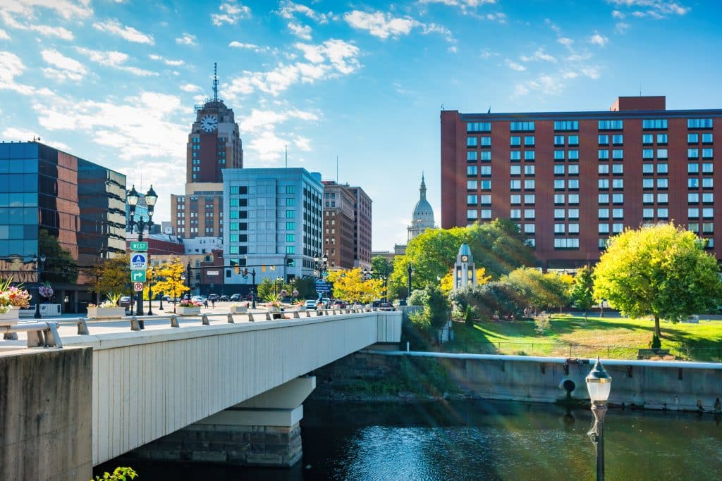 The downtown Lansing skyline and Grand River riverfront, featuring the Boji Tower and pedestrian bridges.