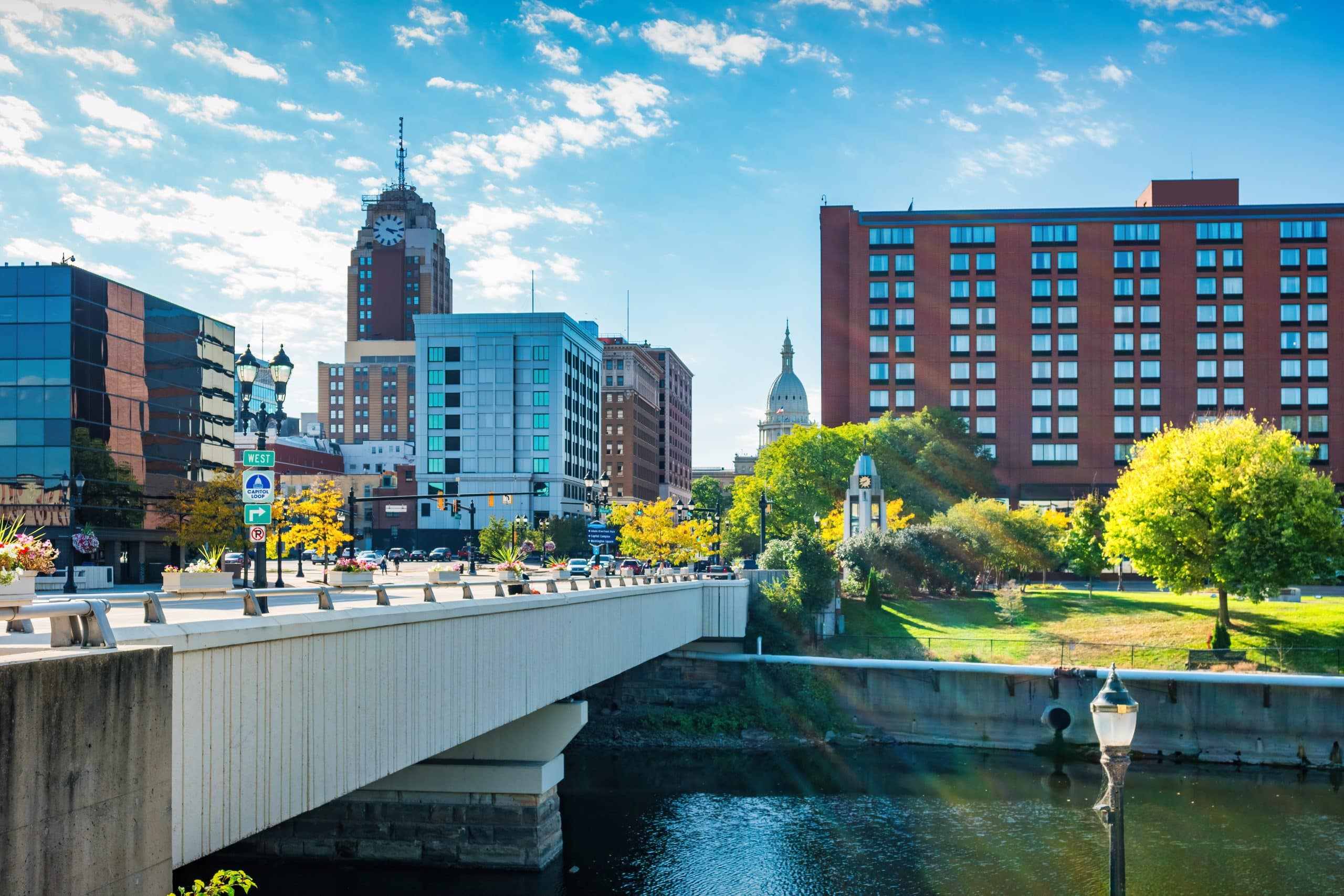 The downtown Lansing skyline and Grand River riverfront, featuring the Boji Tower and pedestrian bridges.